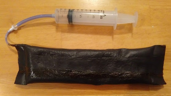 Nitrile rubber pouch filled with coffee grounds; attached syringe is used to pull a vacuum.